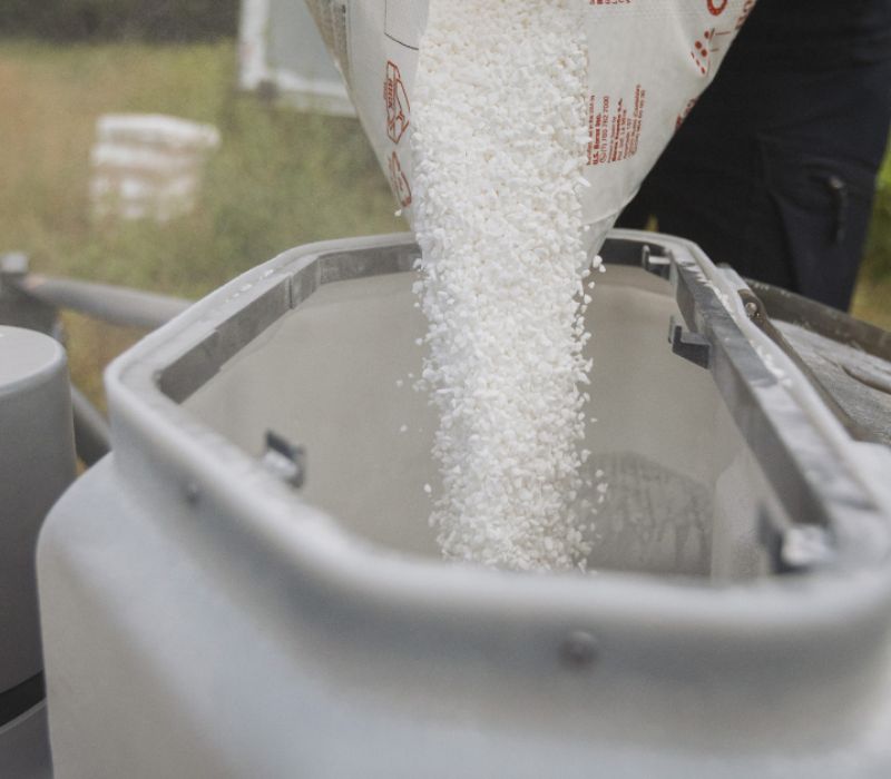 Valkoista rakeista boorilannoitetta kaadetaan säkistä Silvadronesin droonin lannoitesäiliöön metsässä.